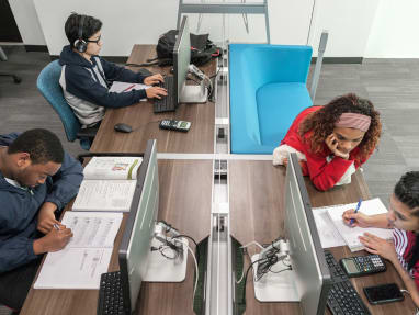Two male students focusing on individual tasks and two female students doing collaborative work